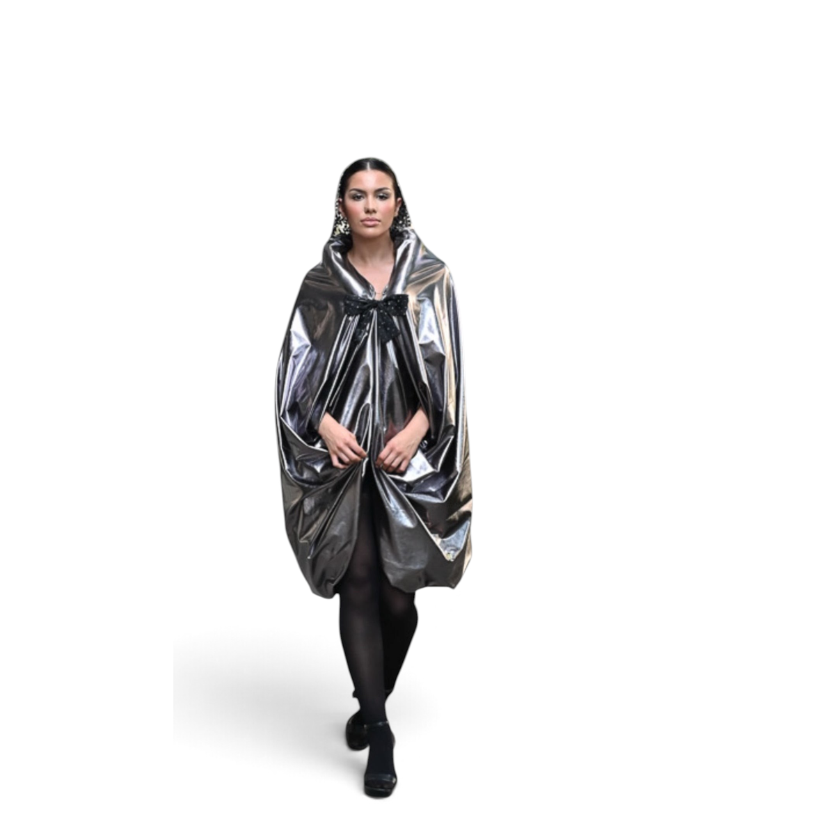 Modelo vestindo capa prateada Dani Levine com silhueta volumosa e laço preto, caminhando em calçada urbana.