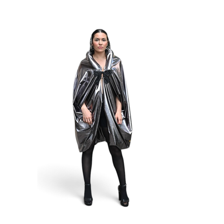 Modelo vestindo capa prateada metálica Dani Levine com laço preto, silhueta volumosa e acabamento brilhante em Paris.
