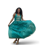 Modelo sorridente usando vestido Dani Levine de linho indiano turquesa com saia em camadas e detalhes metálicos.